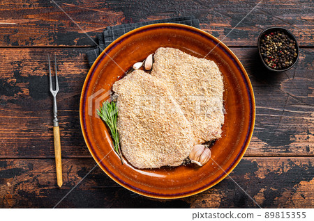 Raw Breaded German Wiener schnitzel on a rustic plate with herbs. Dark wooden background. Top view 89815355