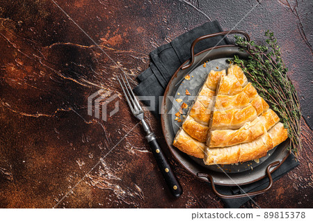 Slices of baked Round Borek cheese pie in kitchen tray with herbs. Dark background. Top view. Copy space 89815378
