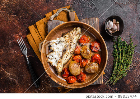 Baked halibut fish with roasted tomato and potato in wooden plate. Dark background. Top view Baked halibut fish with roasted tomato and potato in wooden plate. Dark background. Top view 89815474