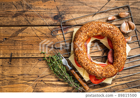 Bagel sandwich with lettuce, tomato, yellow cheese and sausages. Wooden background. Top view. Copy space 89815500