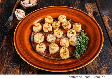 Fried scallops with butter spicy sauce in a plate. Dark wooden background. Top view Fried scallops with butter spicy sauce in a plate. Dark wooden background. Top view 89815528