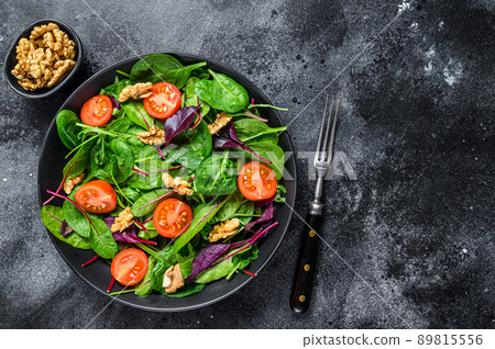 Vegetarian salad with mix leaves mangold, swiss chard, spinach, arugula and nuts in a salad bowl. Black background. Top view. Copy space 89815556
