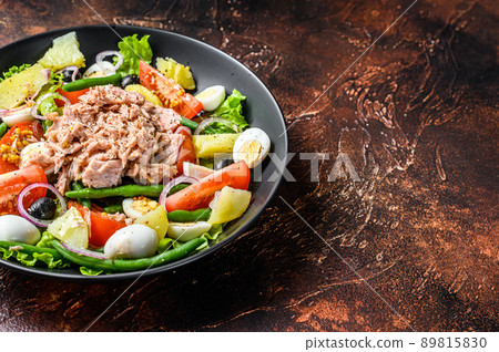 Healthy hearty salad with tuna, green beans, tomatoes, eggs, potatoes and black olives in a plate. Dark background. top view. Copy space 89815830