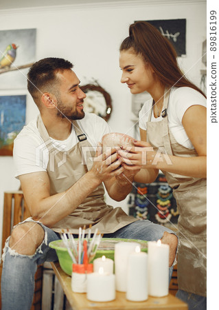 Mutual creative work. Young beautiful couple in casual clothes and aprons. People creating a bowl on a pottery wheel in a clay studio. Mutual creative work. Young beautiful couple in casual clothes and aprons. People creating a bowl on a pottery wheel in a clay studio. 89816199