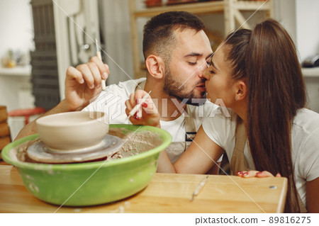 Mutual creative work. Young beautiful couple in casual clothes and aprons. People creating a bowl on a pottery wheel in a clay studio. 89816275