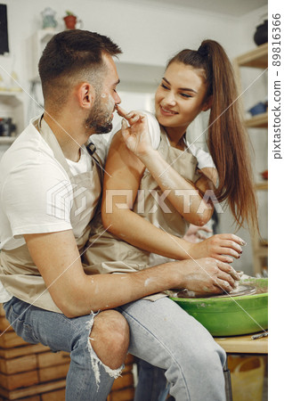 Mutual creative work. Young beautiful couple in casual clothes and aprons. People creating a bowl on a pottery wheel in a clay studio. Mutual creative work. Young beautiful couple in casual clothes and aprons. People creating a bowl on a pottery wheel in a clay studio. 89816366