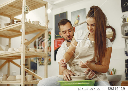Mutual creative work. Young beautiful couple in casual clothes and aprons. People creating a bowl on a pottery wheel in a clay studio. 89816419