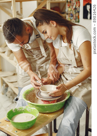 Mutual creative work. Young beautiful couple in casual clothes and aprons. People creating a bowl on a pottery wheel in a clay studio. 89816426