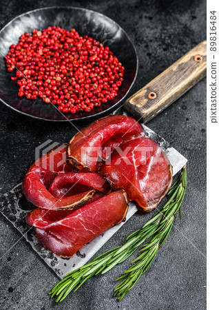 Bresaola dried beef meat sliced on a cleaver. Black background. Top view Bresaola dried beef meat sliced on a cleaver. Black background. Top view 89816484
