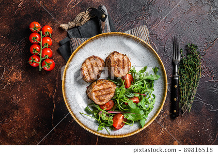 Grilled pork medallions steaks, tenderloin fillet with salad in plate. Dark background. Top view 89816518