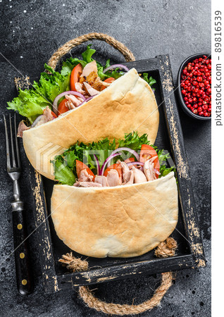 Doner kebab with grilled chicken meat and vegetables in pita bread on a wooden tray. Black background. Top view Doner kebab with grilled chicken meat and vegetables in pita bread on a wooden tray. Black background. Top view 89816539