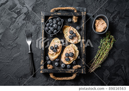 Foie gras toasts, duck liver pate and fresh blueberry in wooden tray. Black background. Top view 89816563