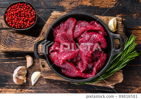Fresh raw diced slices of red beef fiilet meat in cast iron pan. Dark wooden background. Top view Fresh raw diced slices of red beef fiilet meat in cast iron pan. Dark wooden background. Top view 89816581