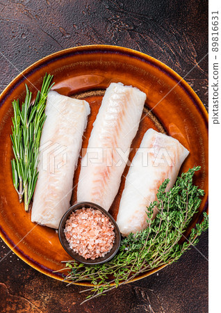 Raw cod loin fillet steaks on rustic plate with thyme and salt. Dark background. Top view 89816631