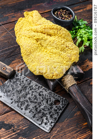 Raw large Viennese schnitzel on a cutting board. Black wooden background. Top view Raw large Viennese schnitzel on a cutting board. Black wooden background. Top view 89816787