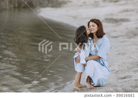 Mom and daughter in identical dresses. Family playing by the river. Mom and daughter in identical dresses. Family playing by the river. 89816881
