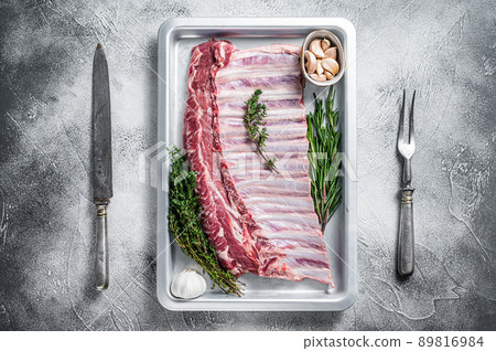 Uncooked raw rack of lamb ribs in baking dish with herbs. White background. Top view 89816984
