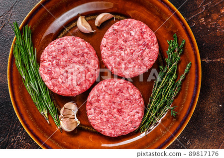Raw burger meat cutlets with mince beef and herbs on a plate. Dark background. Top view Raw burger meat cutlets with mince beef and herbs on a plate. Dark background. Top view 89817176