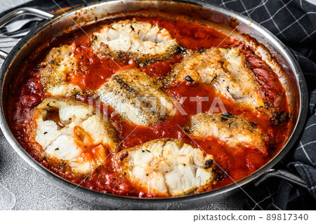 Baked hake white fish with tomato in a pan. White Wooden background. Top view 89817340