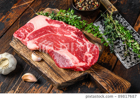 Raw Black Angus prime beef chuck roll steak on a cutting board with cleaver. Dark wooden background. Top view Raw Black Angus prime beef chuck roll steak on a cutting board with cleaver. Dark wooden background. Top view 89817687