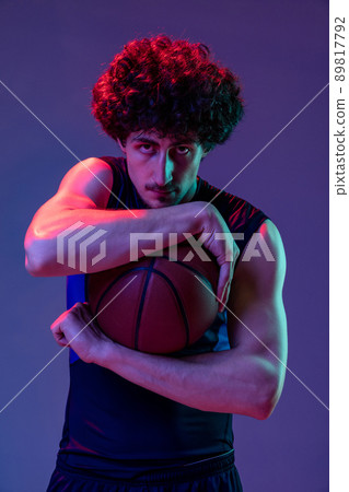 Portrait of young muscular basketball player looking at camera isolated on purple background in neon. Concept of sport, art, creation, competition. Portrait of young muscular basketball player looking at camera isolated on purple background in neon. Concept of sport, art, creation, competition. 89817792