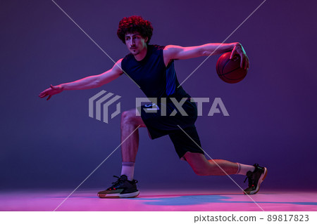 Studio shot of young muscular basketball street player dribbling ball isolated on purple background in neon. Concept of sport, art, creation, competition. Studio shot of young muscular basketball street player dribbling ball isolated on purple background in neon. Concept of sport, art, creation, competition. 89817823