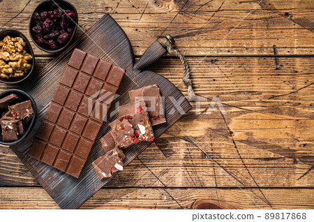 Dark chocolate bar with hazelnuts, peanuts, cranberries and freeze dried raspberries on a wooden board. wooden background. Top view. Copy space Dark chocolate bar with hazelnuts, peanuts, cranberries and freeze dried raspberries on a wooden board. wooden background. Top view. Copy space 89817868