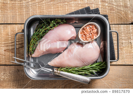 Raw chicken breast fillet in kitchen tray with thyme and rosemary. Wooden background. Top view Raw chicken breast fillet in kitchen tray with thyme and rosemary. Wooden background. Top view 89817870