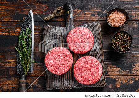 Raw steak burgers patties with ground beef and thyme on a wooden cutting board. Dark Wooden background. Top view Raw steak burgers patties with ground beef and thyme on a wooden cutting board. Dark Wooden background. Top view 89818205