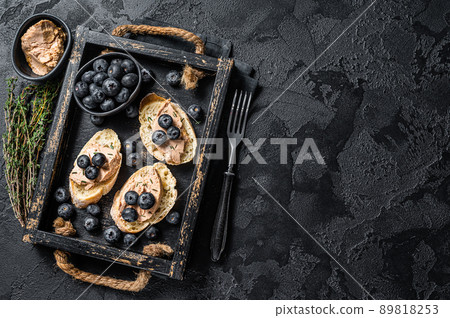 Foie gras toasts, duck liver pate and fresh blueberry in wooden tray. Black background. Top view. Copy space 89818253