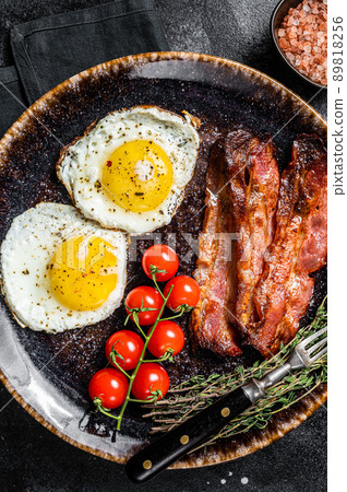 Breakfast with fried eggs and bacon with herbs in plate. Black background. Top view 89818256