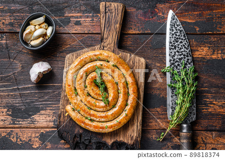 BBQ spiral sausage from pork and beef meat on a wooden cutting board. Dark wooden background. Top view BBQ spiral sausage from pork and beef meat on a wooden cutting board. Dark wooden background. Top view 89818374
