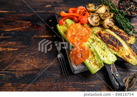 Grilled vegetables bell pepper, zucchini, eggplant and tomato with dry herbs on a wooden board. Dark wooden background. Top view. Copy space 89818754
