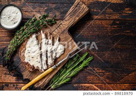 Roast fillet beef meat steak with peppercorn sauce on wooden board. Dark wooden background. Top view. Copy space 89818970