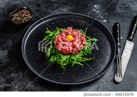 Beef tartar with a quail egg served on a black stone plate.. Black background. Top view Beef tartar with a quail egg served on a black stone plate.. Black background. Top view 89818976
