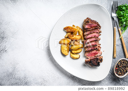 Sliced striploin steak with potato. White background. Top view. Copy space 89818992