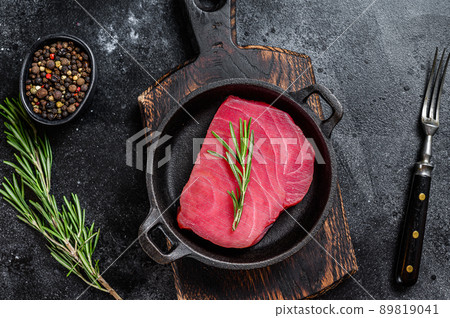 Fresh Raw tuna steak with rosemary in a pan. Black background. Top view Fresh Raw tuna steak with rosemary in a pan. Black background. Top view 89819041