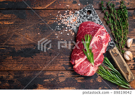 Raw Chuck eye roll Black Angus prime beef steak on butcher cleaver. Dark wooden background. Top view. Copy space 89819042