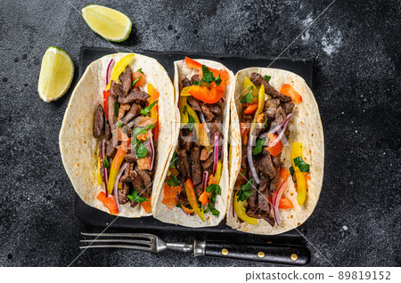 Mexican tacos shells with beef meat, onion, tomato and sweet pepper. Black background. Top view Mexican tacos shells with beef meat, onion, tomato and sweet pepper. Black background. Top view 89819152