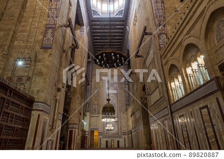 Interior of al Refai mosque with old decorated bricks stone wall, colored marble decorations, wooden ornate ceiling, big brass chandeliers, and wooden latticework door, Cairo, Egypt 89820887