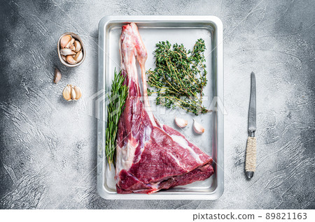 Uncooked Raw goat or lamb leg with herbs in baking tray. White background. Top view 89821163