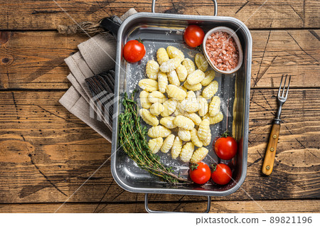 Uncooked Raw potato gnocchi in kitchen steel tray with herbs. Wooden background. Top view 89821196