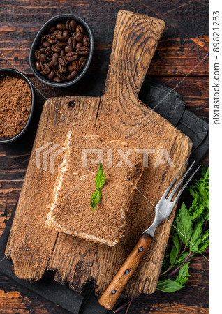 Italian dessert Tiramisu cake with cocoa and mint on a wooden board. Dark Wooden background. Top view 89821233