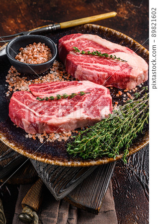 Chuck eye Roll beef steaks, raw meat on a plate with thyme and herbs. Dark background. Top view 89821602
