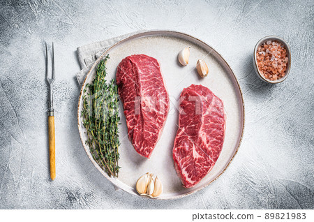 Raw Oyster Top Blade or flat iron roast beef meat steaks on a plate with herbs. White background. Top View Raw Oyster Top Blade or flat iron roast beef meat steaks on a plate with herbs. White background. Top View 89821983