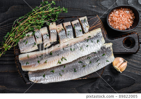 Sliced salted herring fish fillet on a wooden board. Black wooden background. Top view 89822005