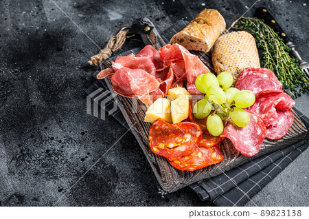 Cold meat plate, charcuterie - traditional Spanish tapas on a wooden board with bread and grape. Black background. Top view. Copy space 89823138
