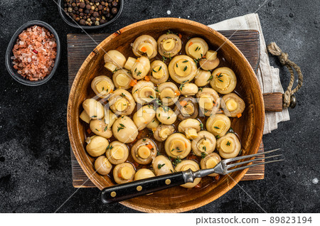 Pickled Marinated mushrooms champignons in a wooden plate. Black background. Top view 89823194