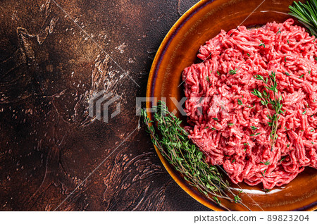 Raw ground beef or veal meat on a rustic plate with herbs. Dark background. Top view. Copy space Raw ground beef or veal meat on a rustic plate with herbs. Dark background. Top view. Copy space 89823204