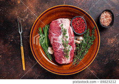 Raw round beef meat prime cut for roast on a rustic plate with herbs. Dark background. Top view 89823212